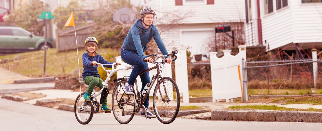 Family bike portrait with little happy boy ride on a tow tandem bicycle attached to father on urban street side view